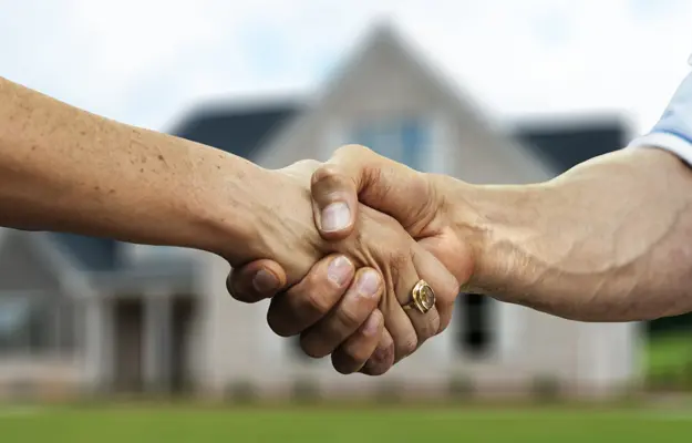 Deux mains entrelacées dans une poignée de main devant une maison